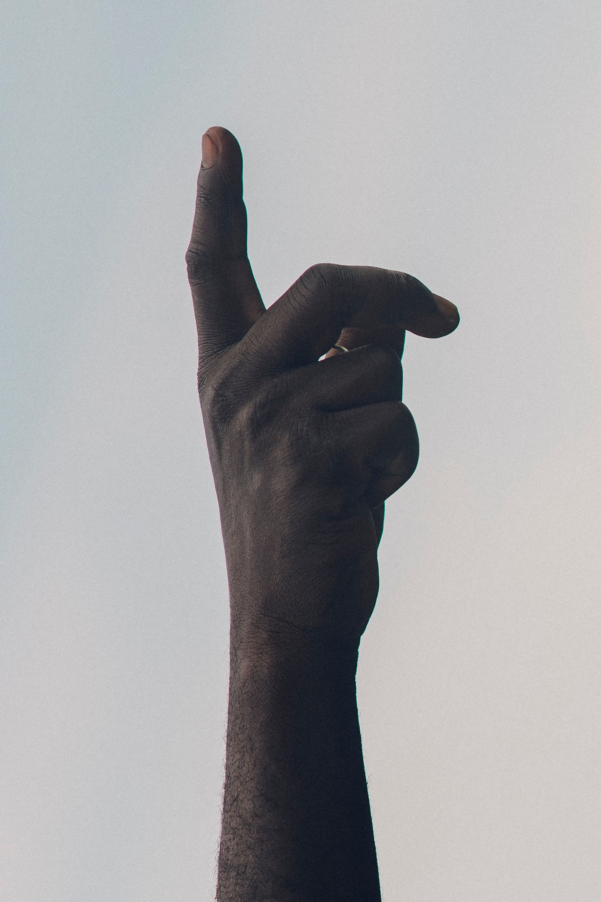 blue-grey background with black person's hand pointing upward toward the sky